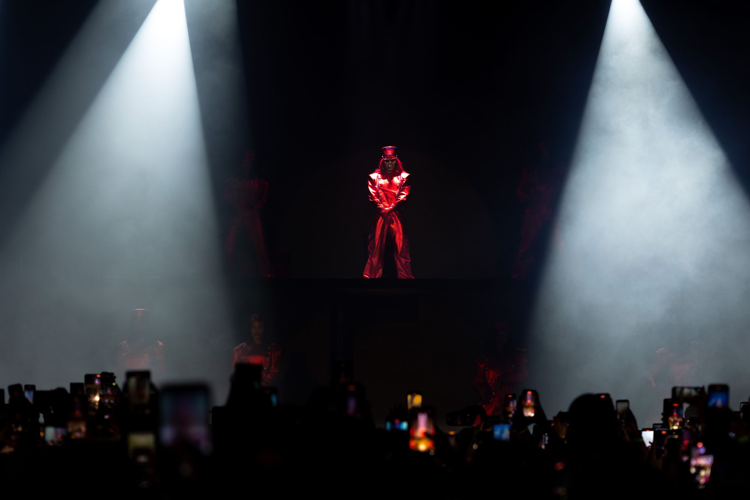 Solo performer stands in dramatic spotlight on dark stage with crowd below.