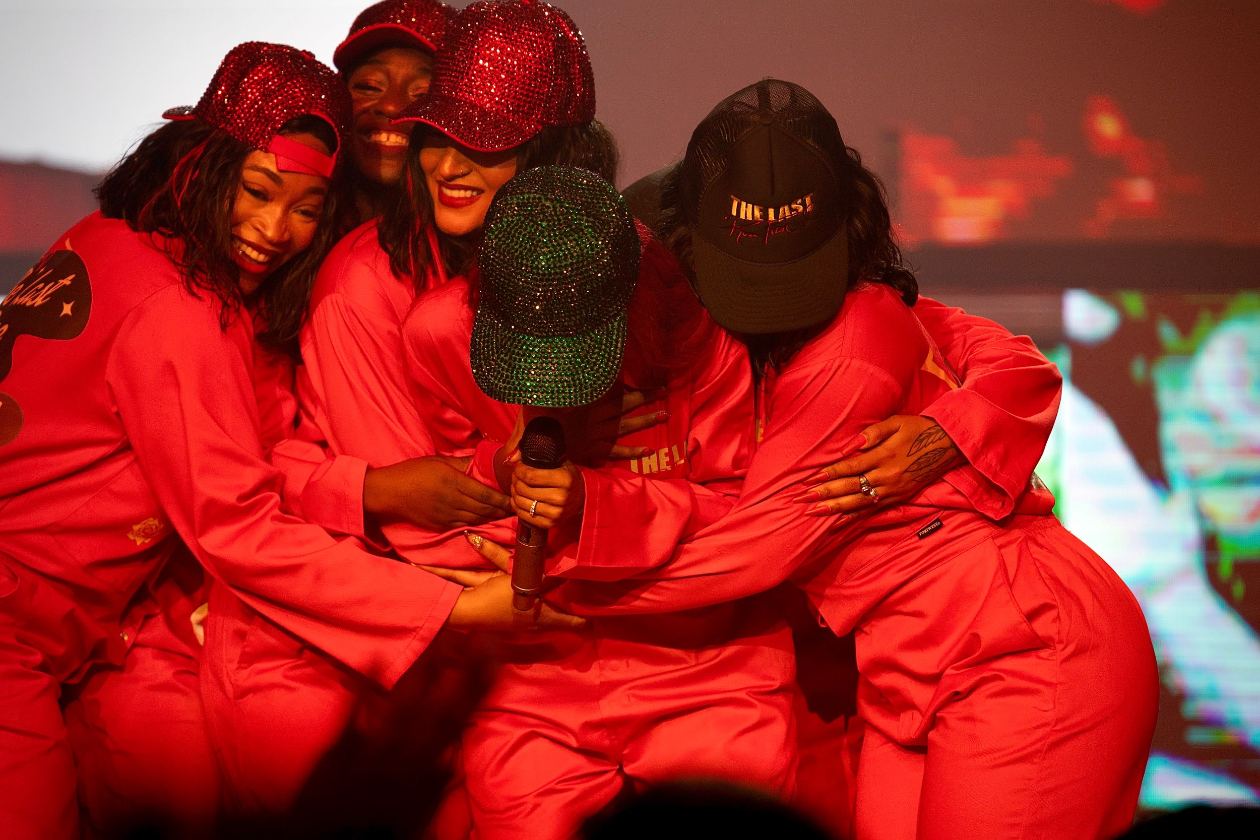 Group in matching red outfits huddle together during stage performance.