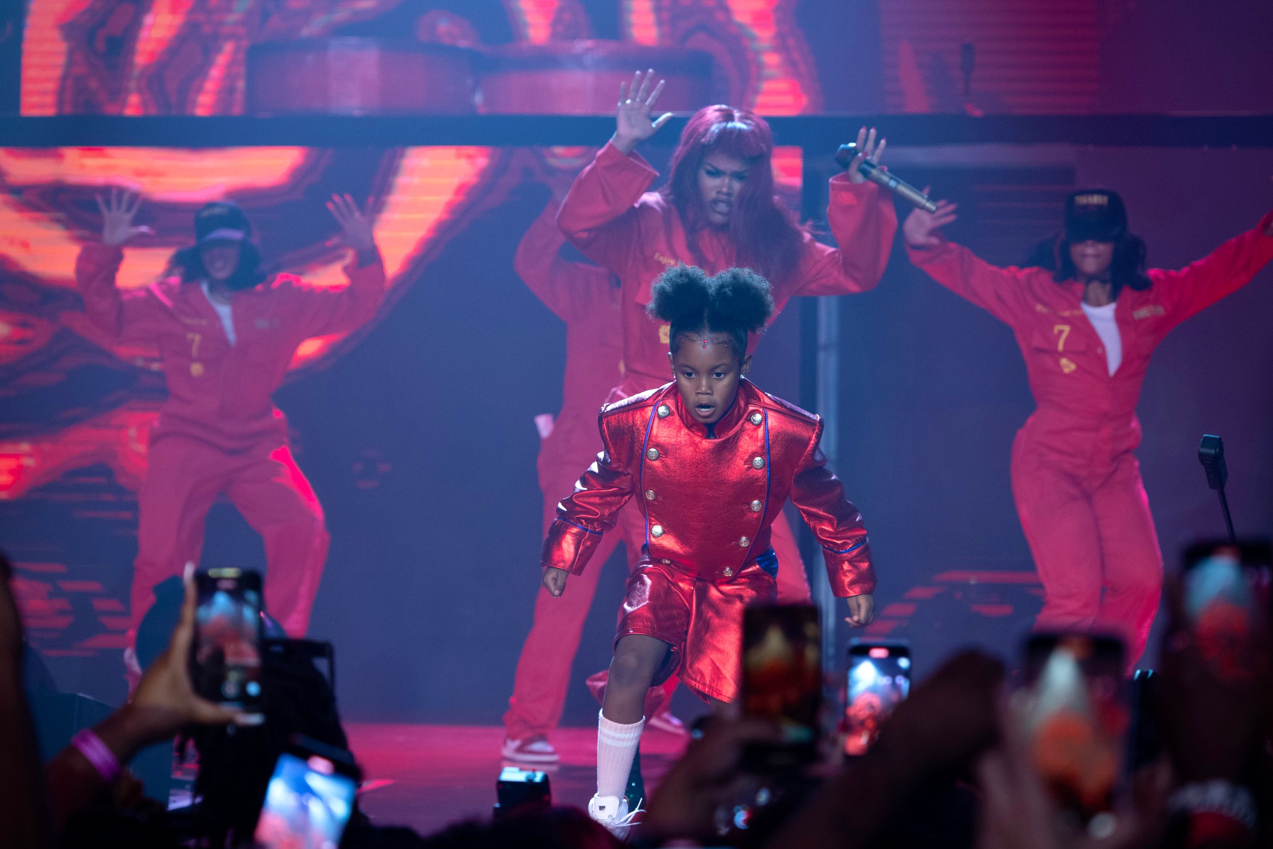Dancers in bright red costumes perform synchronized routine on illuminated stage.