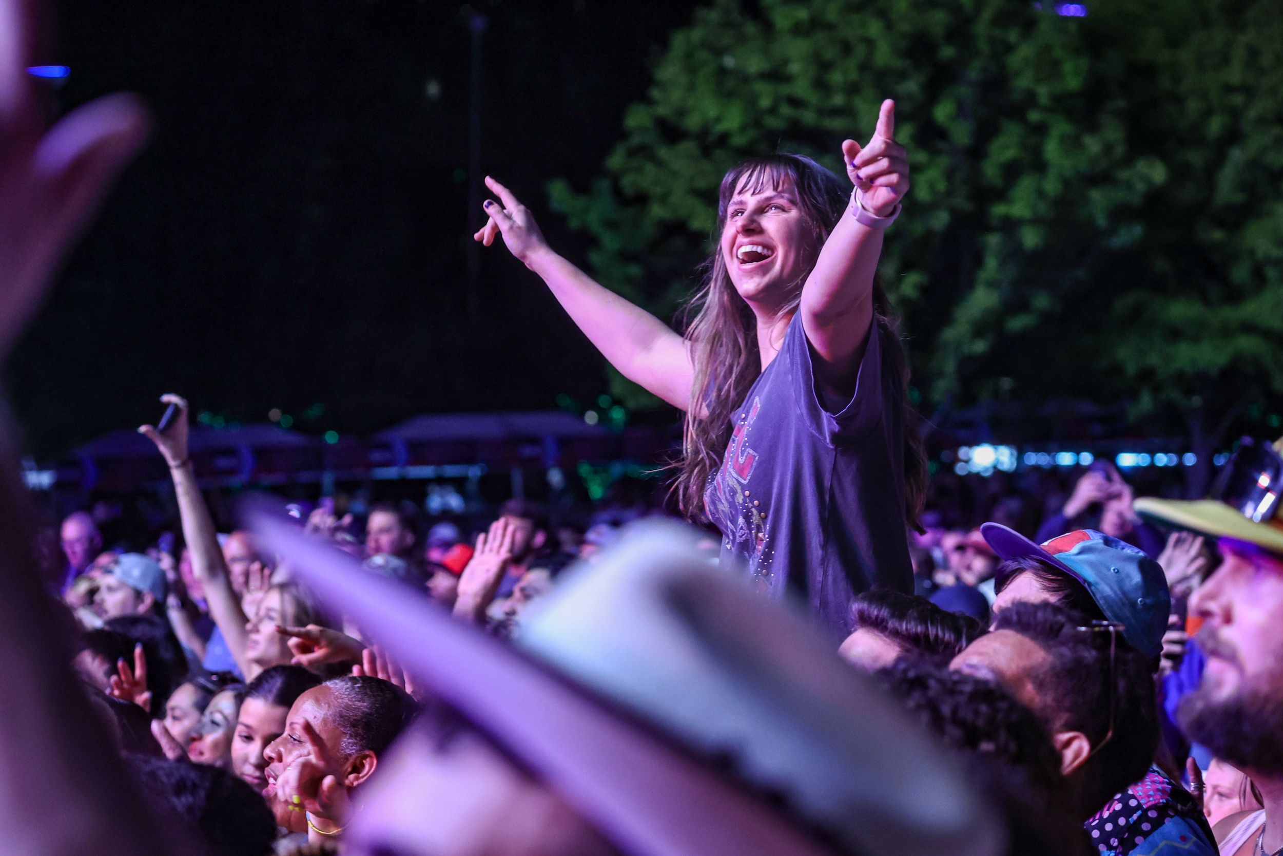 Enthusiastic concert crowd member raises hands in celebration during outdoor music festival.