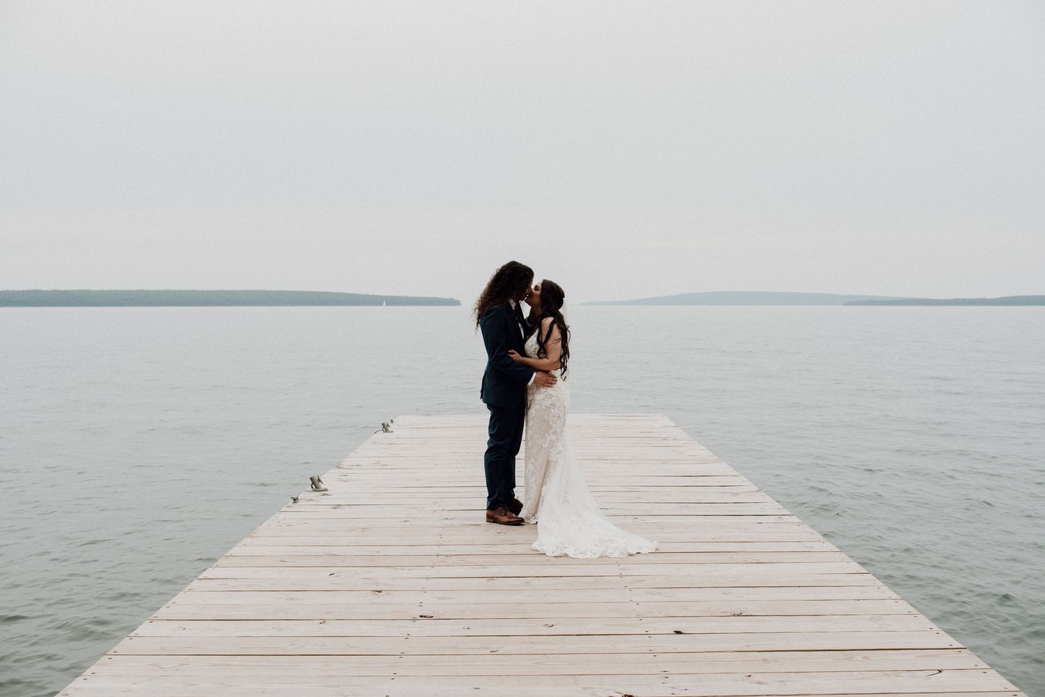 a bride and groom stand on a dock kissing on the lake superior at Madeline Island, Wisconsin