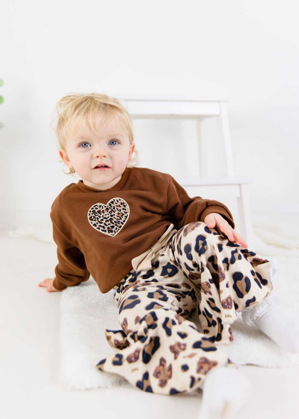 Baby wearing brown sweater with leopard print pants in studio setting.