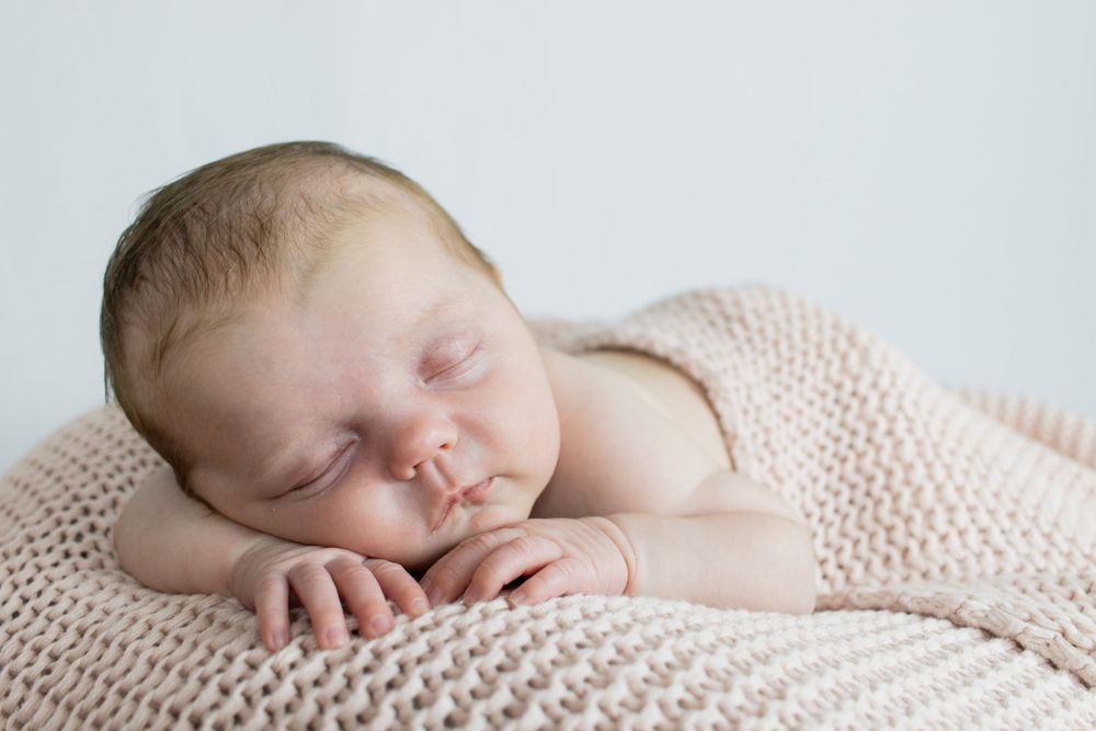 Peaceful sleeping newborn baby on soft knit blanket during professional photo session.
