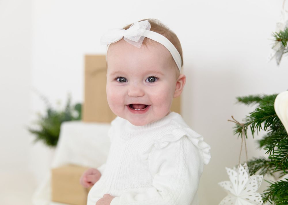 Holiday themed baby photography session with white decorations and Christmas tree.