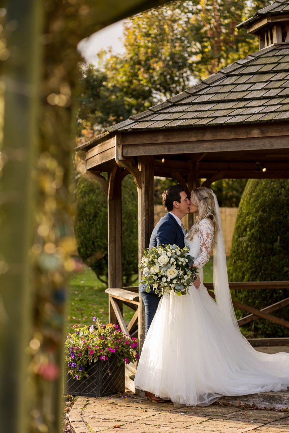 Romantic wedding couple embracing in a garden gazebo with white and yellow floral arrangements.