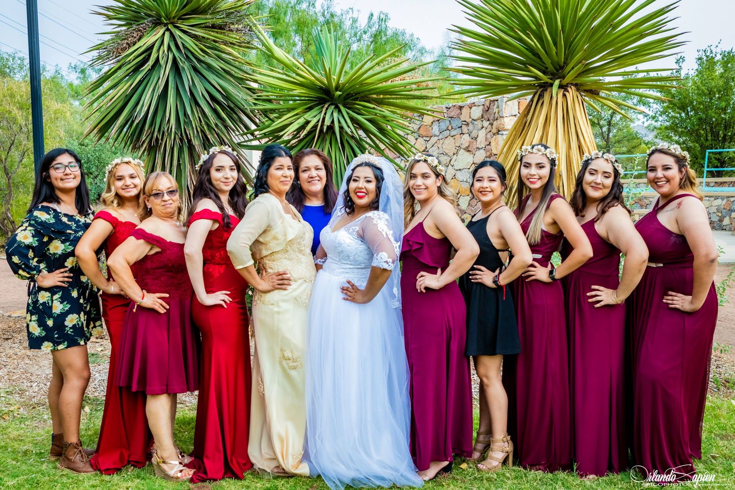 Bridesmaids in burgundy and light blue dresses posing outdoors with palm trees.