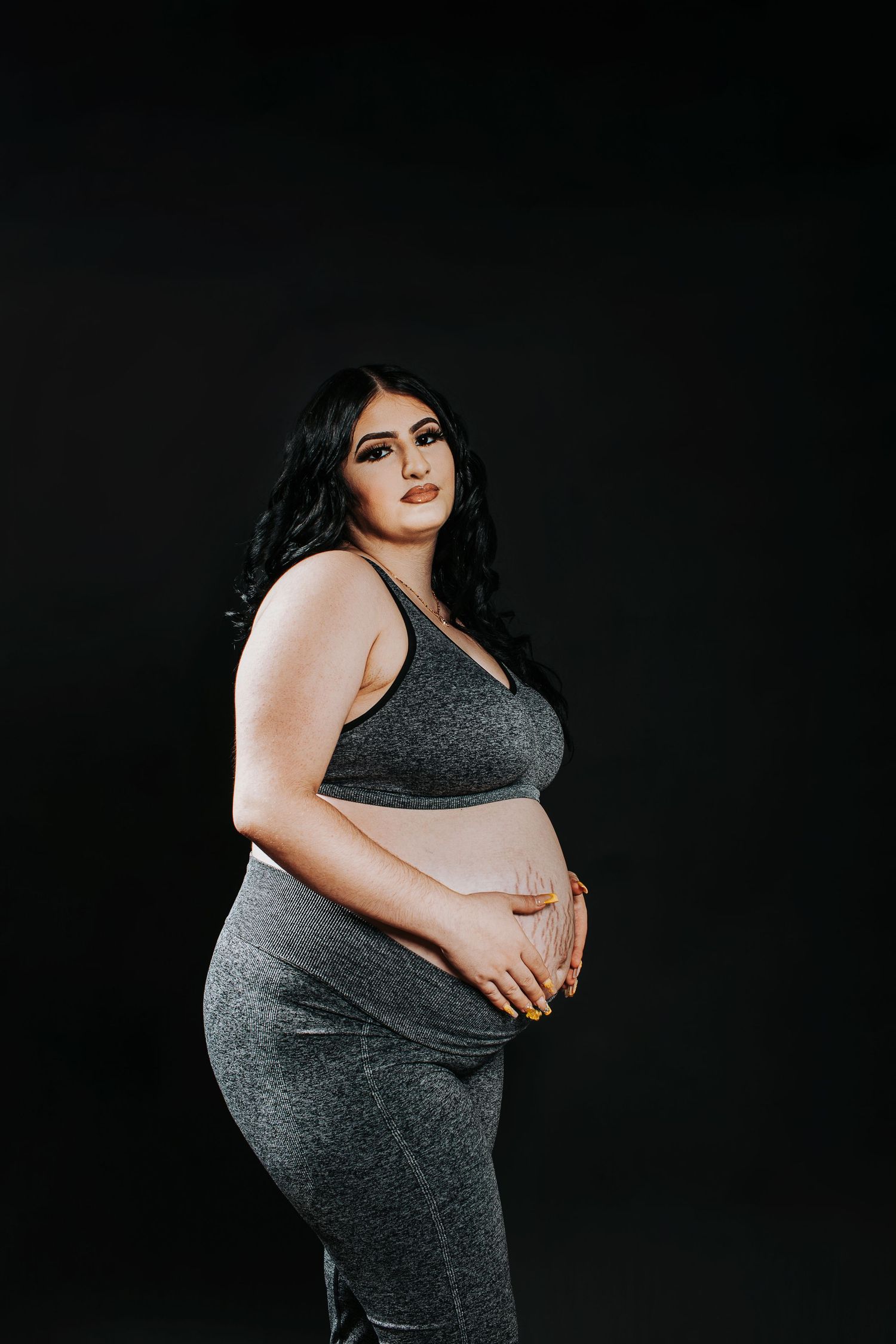 Artistic maternity photoshoot against black background highlighting the baby bump.