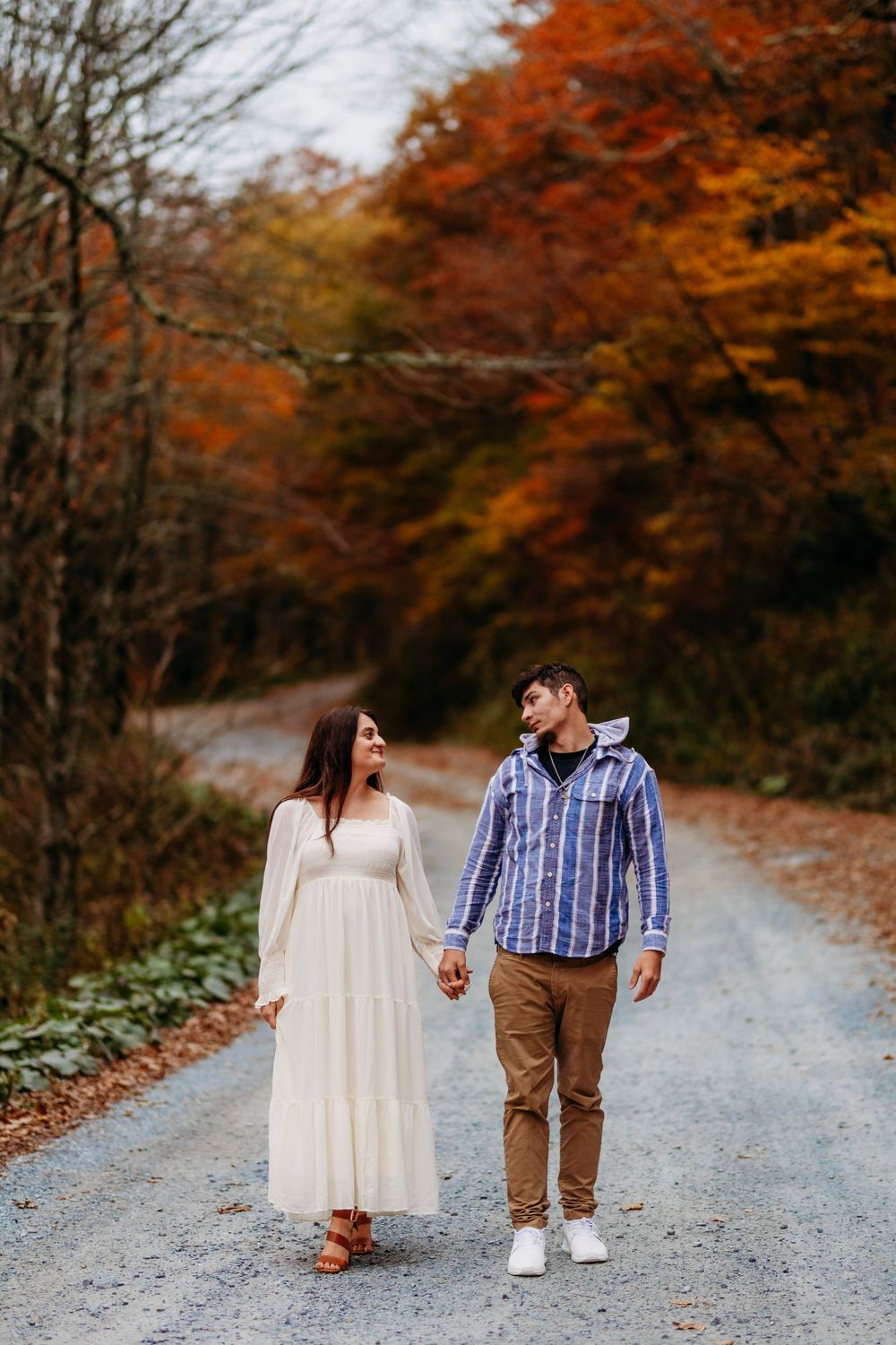 Couple walking hand in hand down a gravel road lined with vibrant fall foliage.