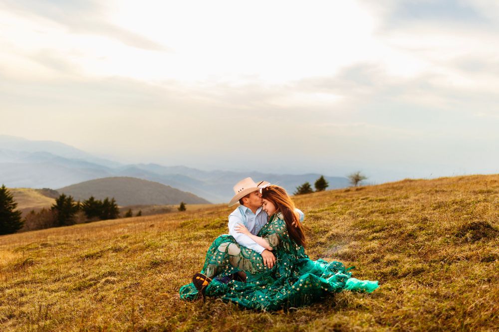 Couple sitting closely together in golden mountain meadow under soft sunset sky.
