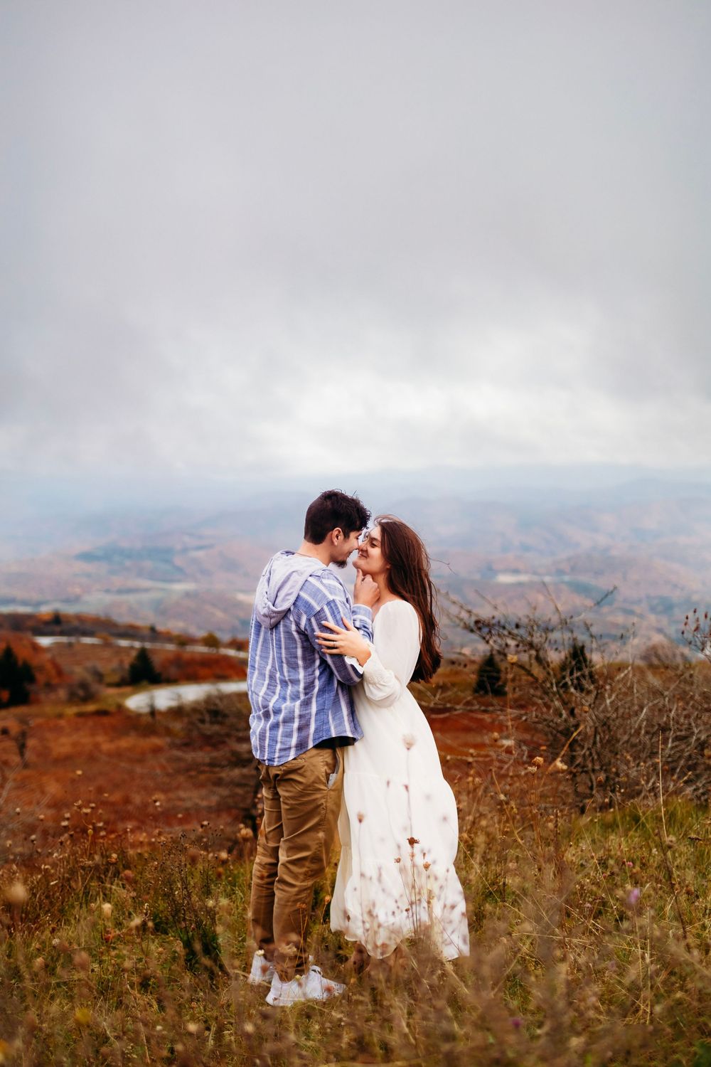 Romantic couple embracing on a hilltop with breathtaking autumn valley panorama below.