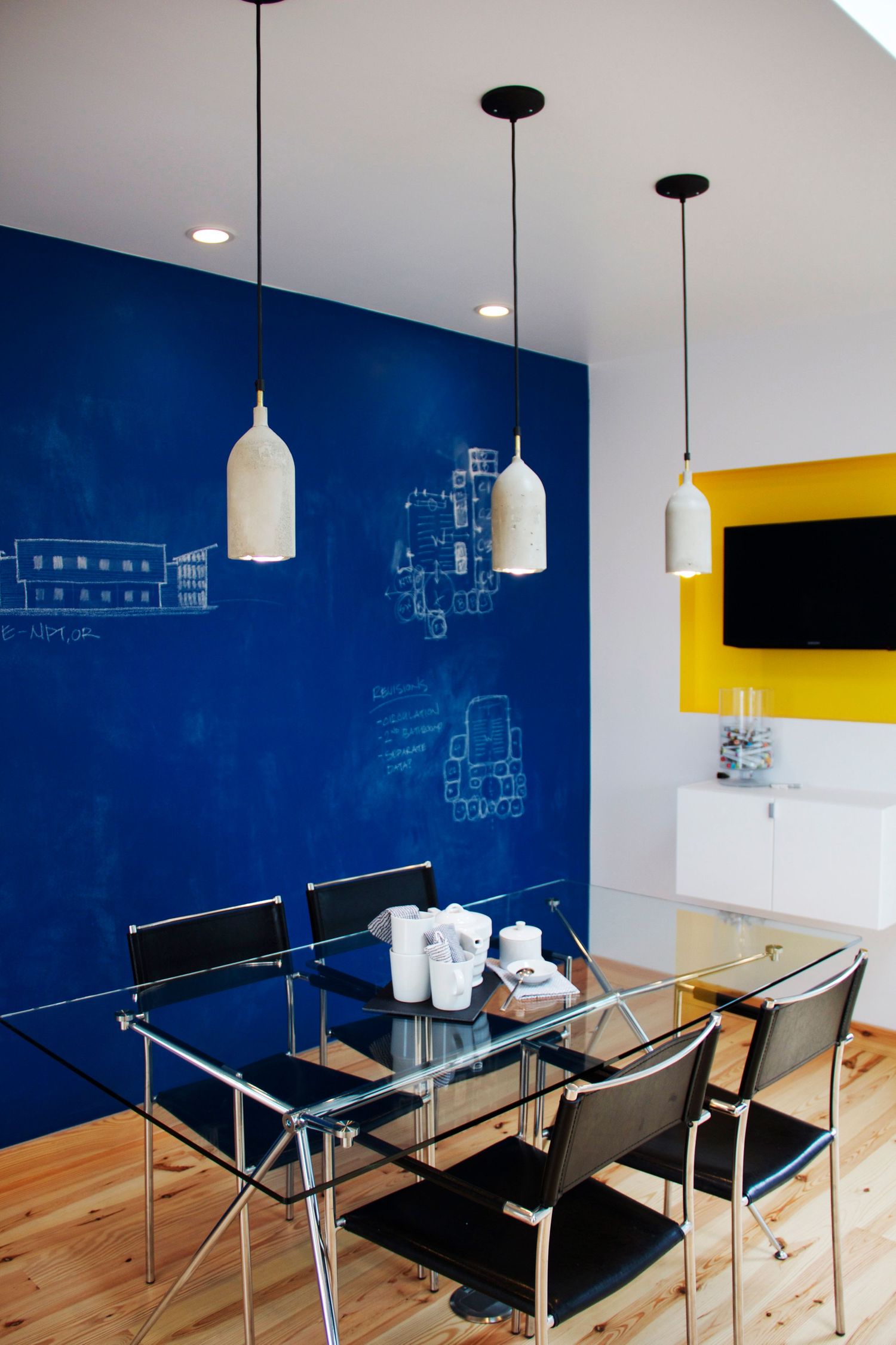 Modern dining area with blue accent wall, white pendant lights, and glass table.