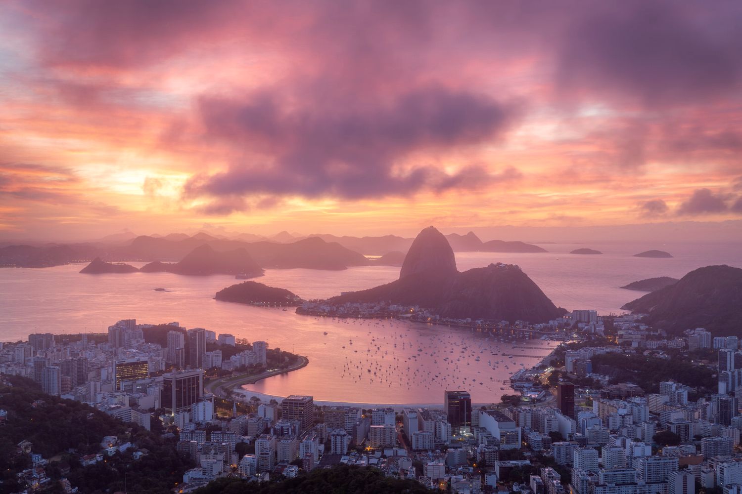 Sugarloaf Mountain and Rio de Janeiro cityscape illuminated by dramatic purple sunset.