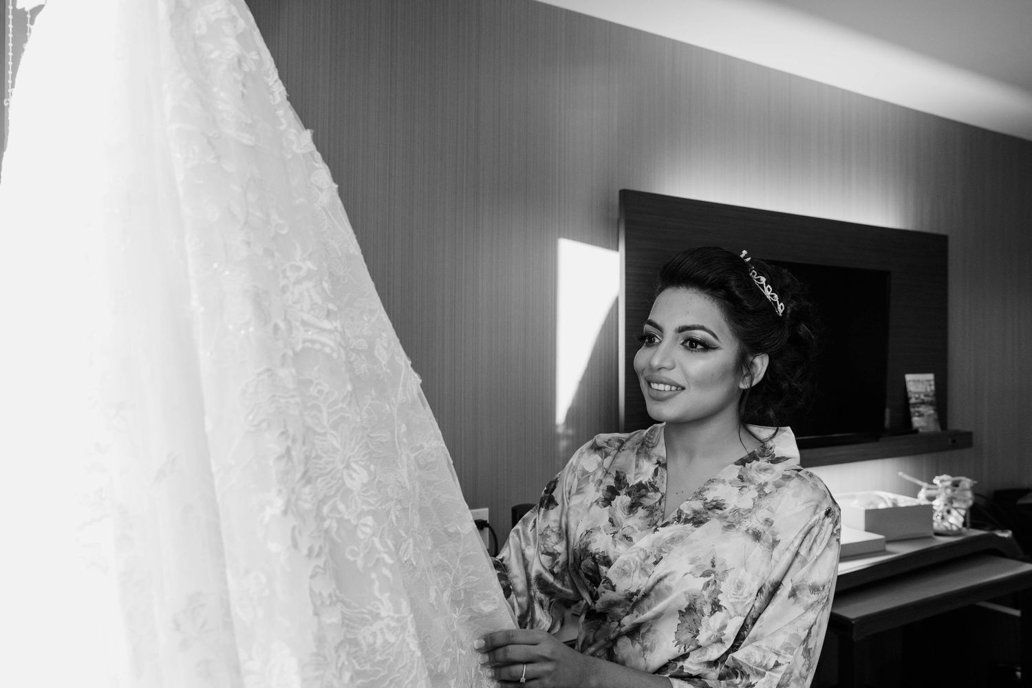 Wedding Dress on a hanger against wall that is bright white and Bride look in to her dress.