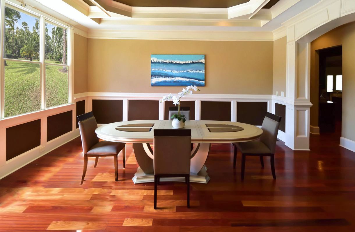 Modern dining room with hardwood floors, white trim, and beige walls featuring round table and mounted TV.