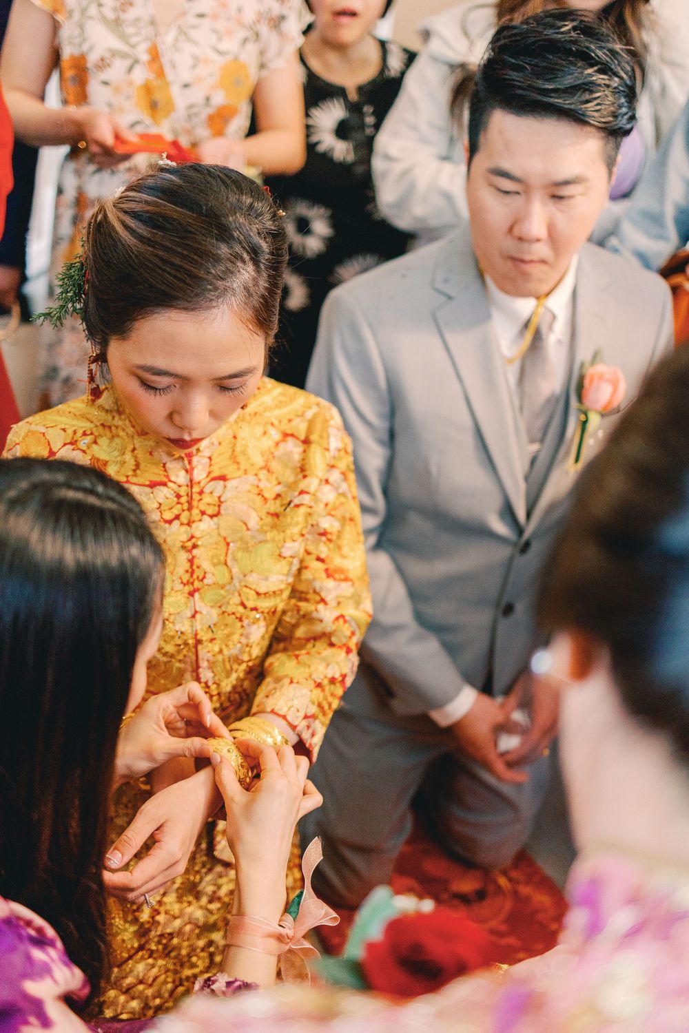Bride in golden traditional dress and groom in grey suit participate in a wedding ceremony surrounded by guests.