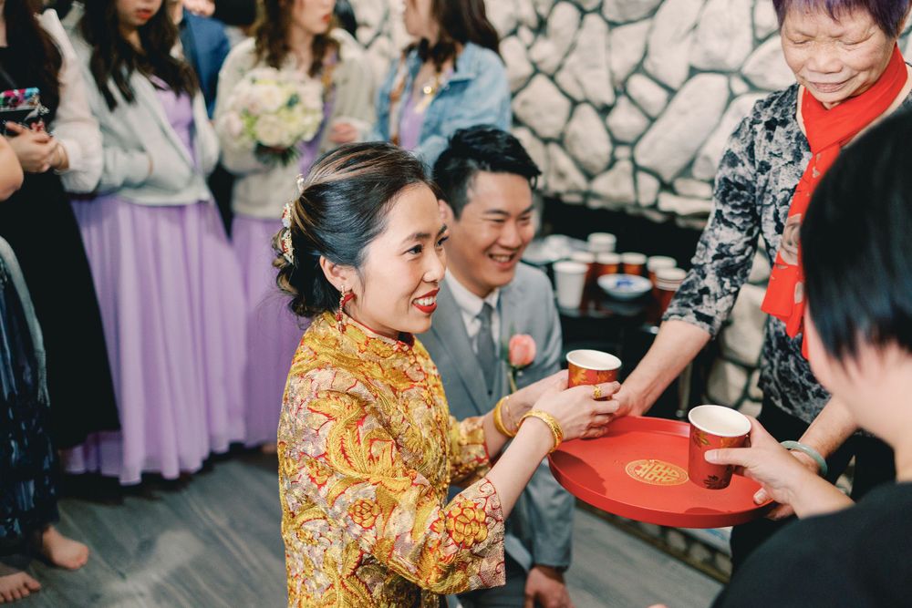 A bride in a golden floral qipao serves tea to family members during a traditional Chinese wedding tea ceremony.