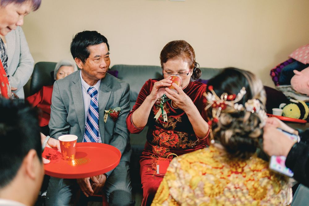 Young boy in tie drinking from cup at social gathering with people around him.