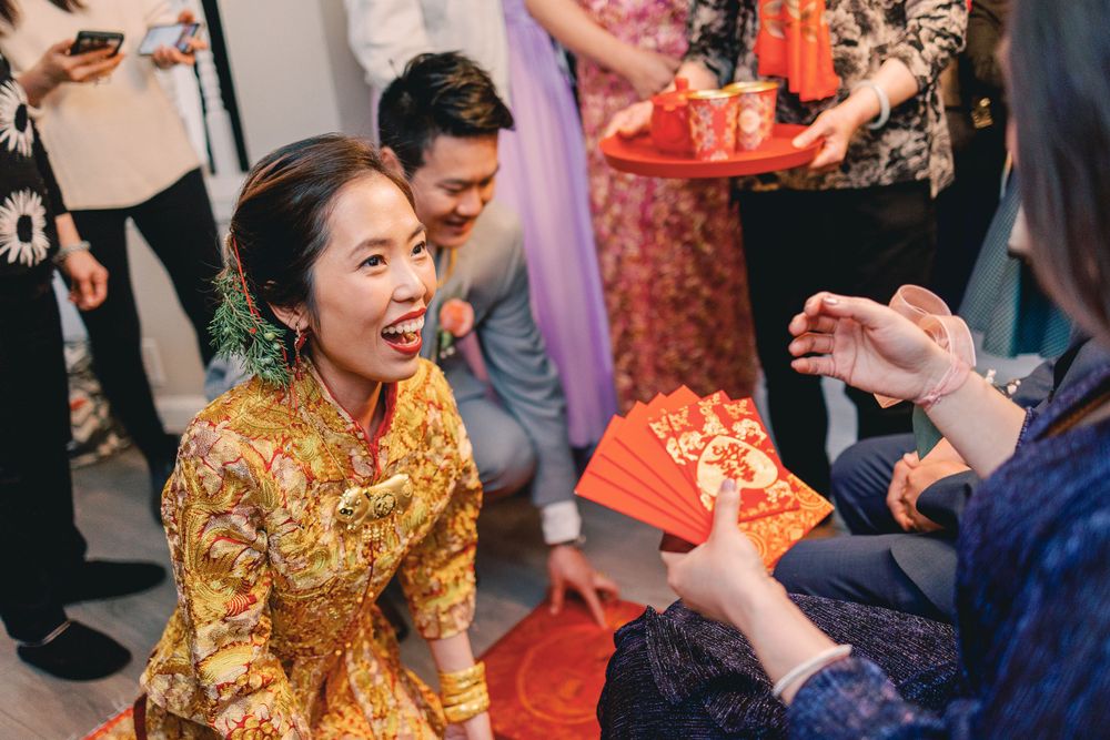 A smiling bride in a golden traditional dress receives red envelopes during a Chinese wedding tea ceremony celebration.
