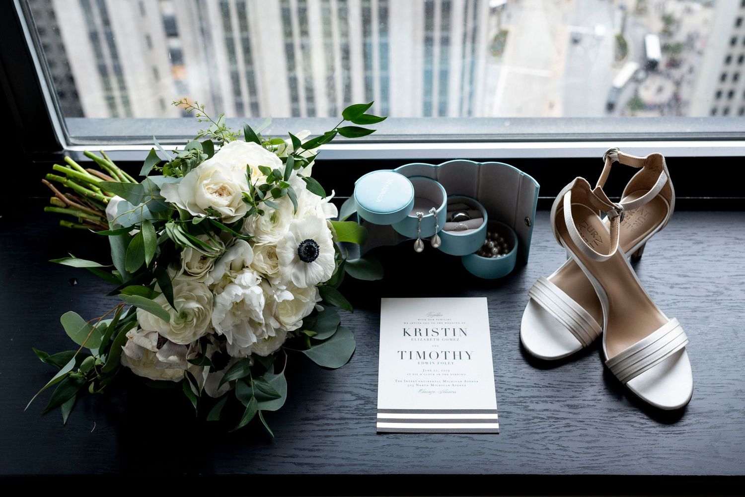 Still life of a brides shoes, jewelry, wedding invitation and boquette of flowers on a Chicago hotel windowsill.