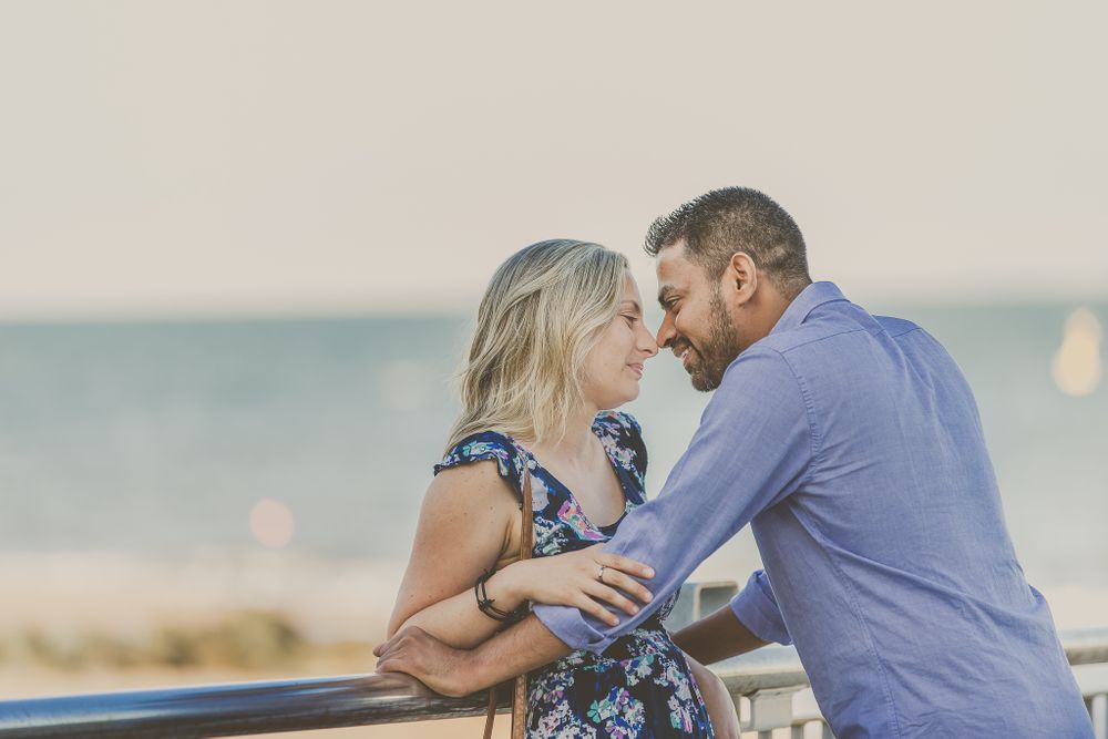 Intimate moment between couple on beachside pier during sunset.