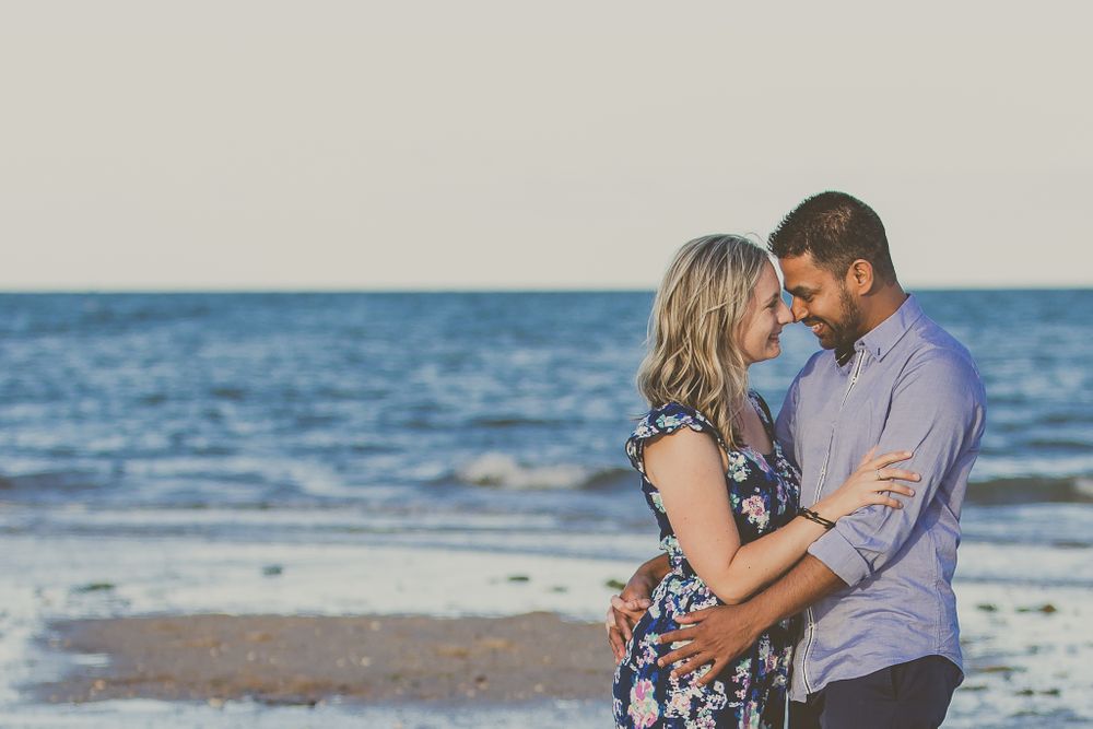 Couple in loving embrace on beach with blue ocean horizon in background.