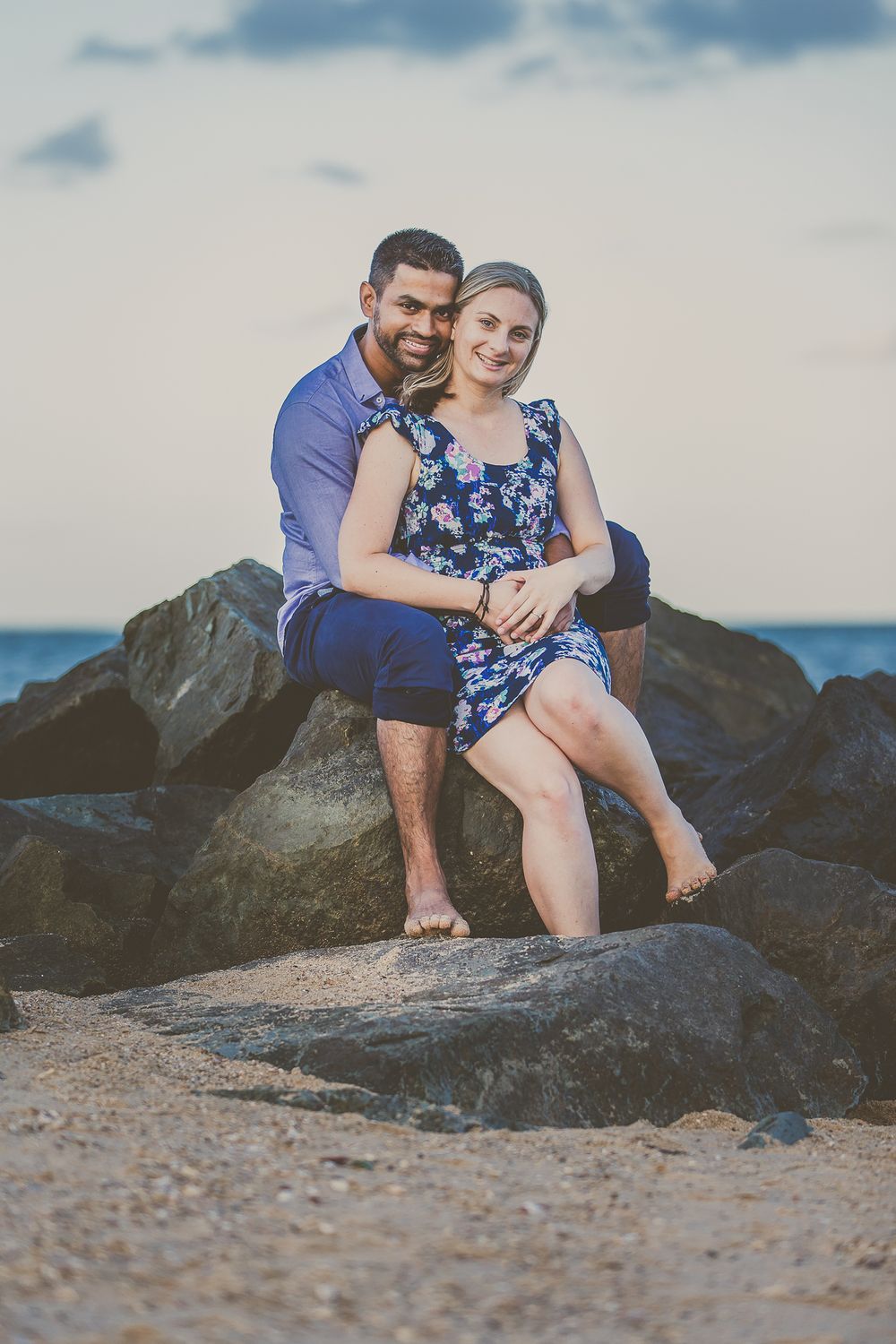 Couple sitting together on rocky beach outcrop with ocean view.
