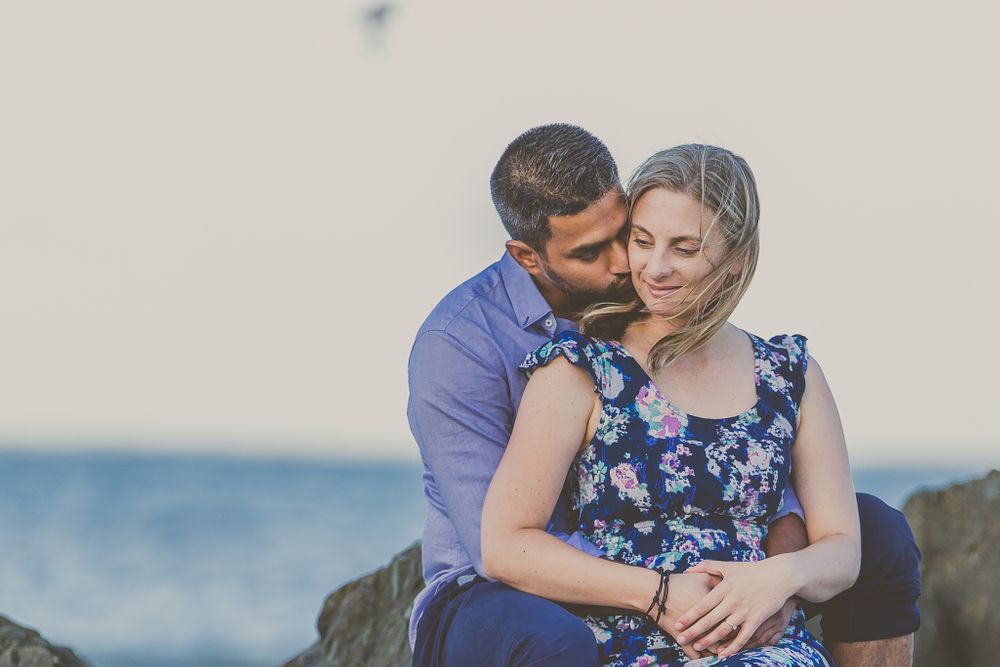 Close romantic moment shared between couple on rocky beach during sunset.