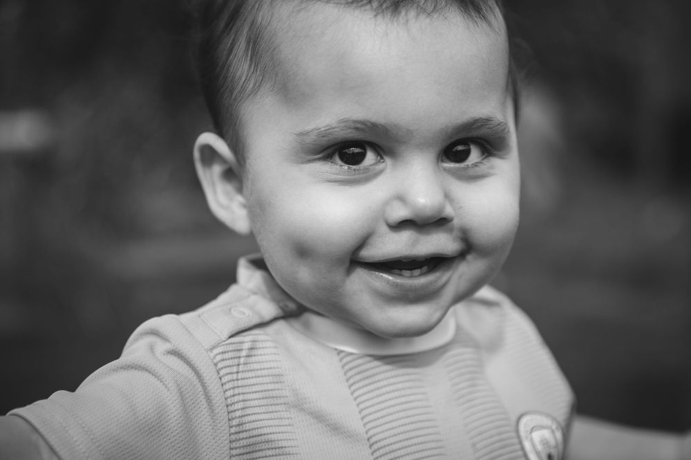 Close-up black and white portrait of a smiling toddler in a sweater.