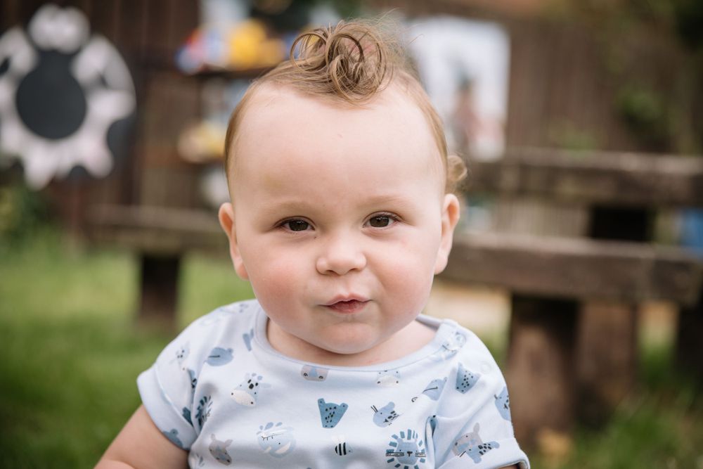 Baby in floral print outfit smiling outdoors with playground in background.