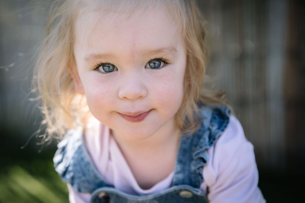 Portrait of a child in denim overalls and pink shirt with bright eyes and gentle smile.