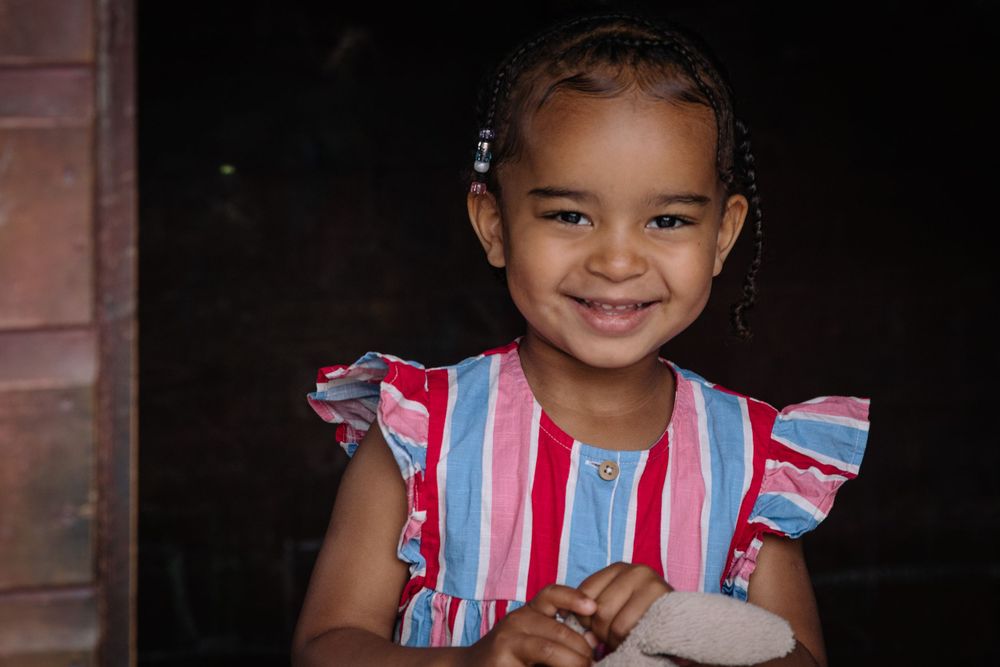 Young person wearing colorful striped dress smiles brightly against dark background.