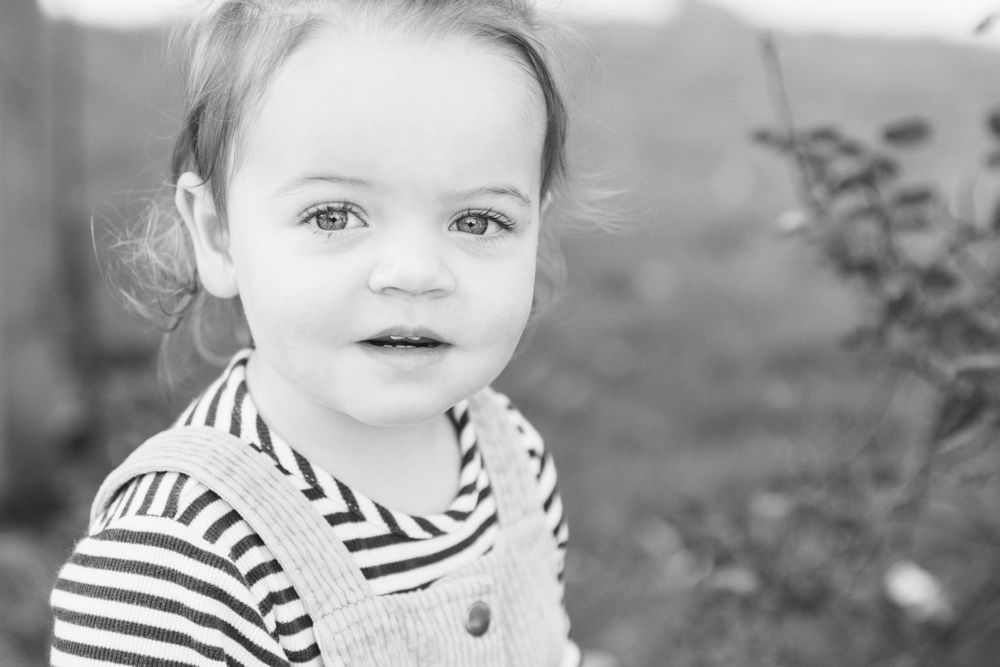 Black and white portrait of a small child in striped overalls looking at the camera.