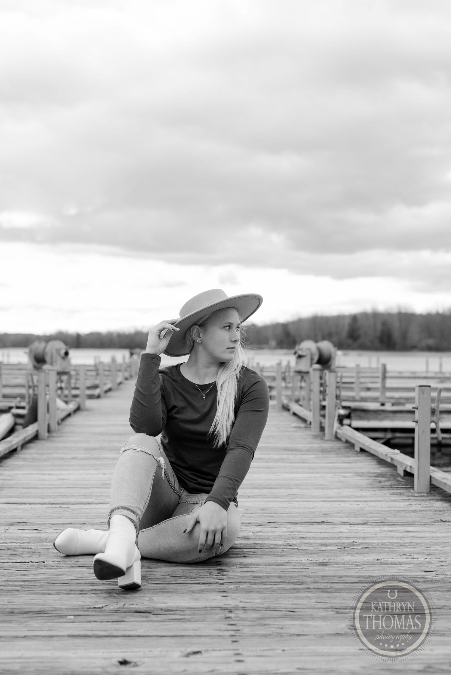Person in hat sitting on wooden dock in black and white photograph.