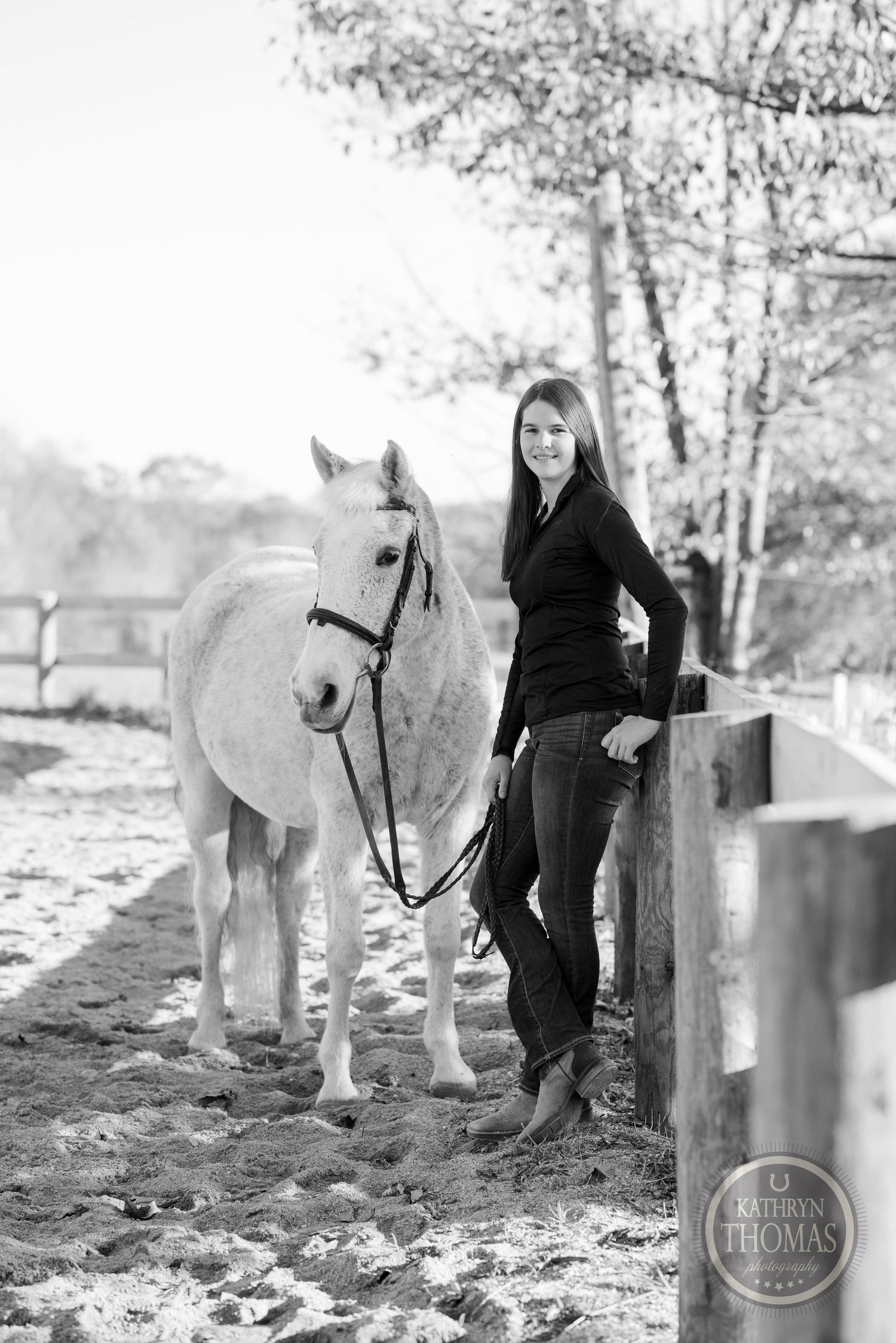A black and white portrait captures a white horse and companion by a rustic fence.