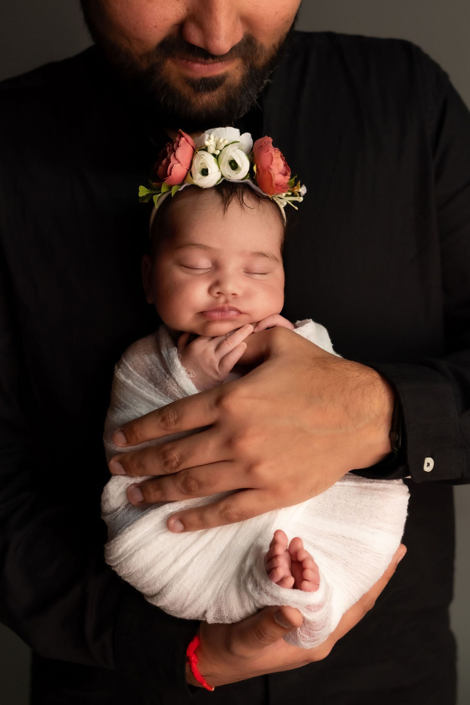 Studio portrait session of a newborn baby wrapped in white with floral accessories.