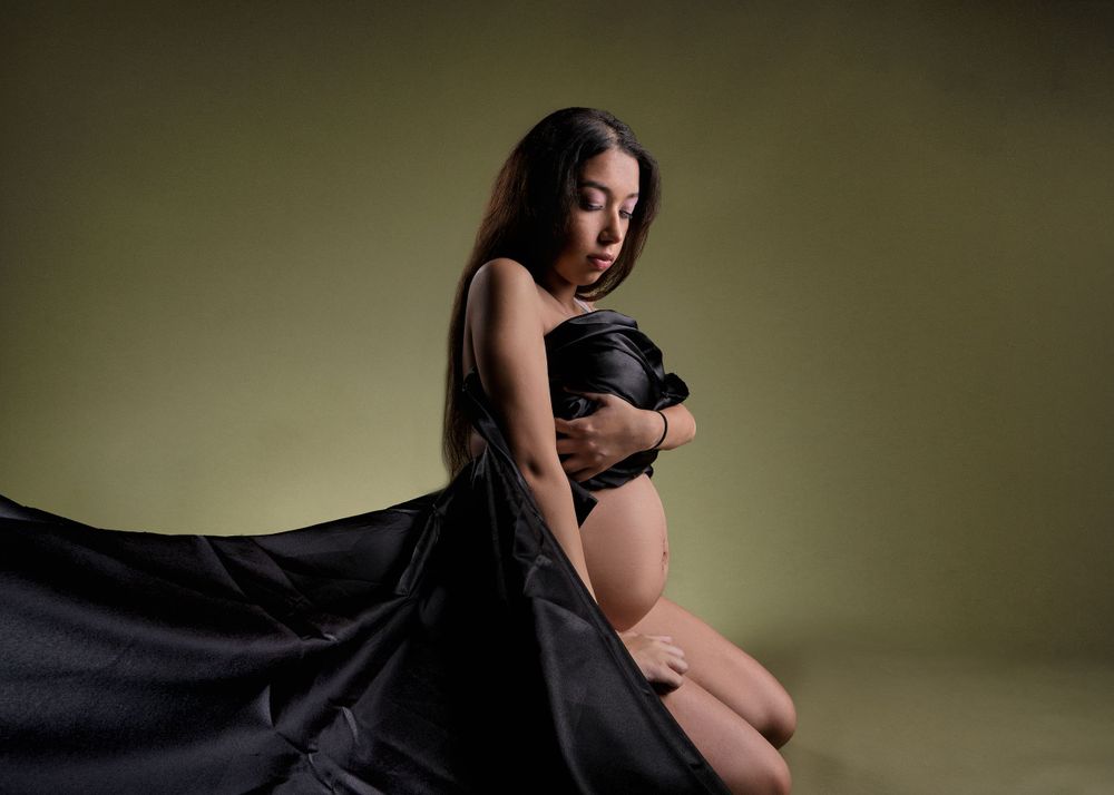 Artistic maternity photo with dramatic black fabric draping.