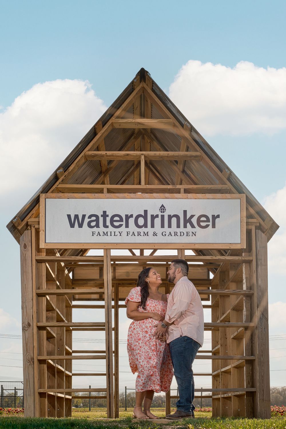 Couple embracing under rustic wooden structure with Waterdrinker Family Farm sign.