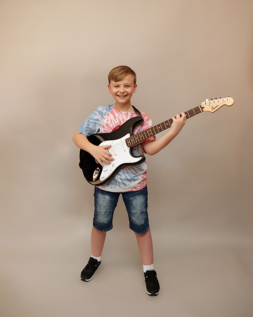 Young musician poses with electric guitar against neutral studio background.