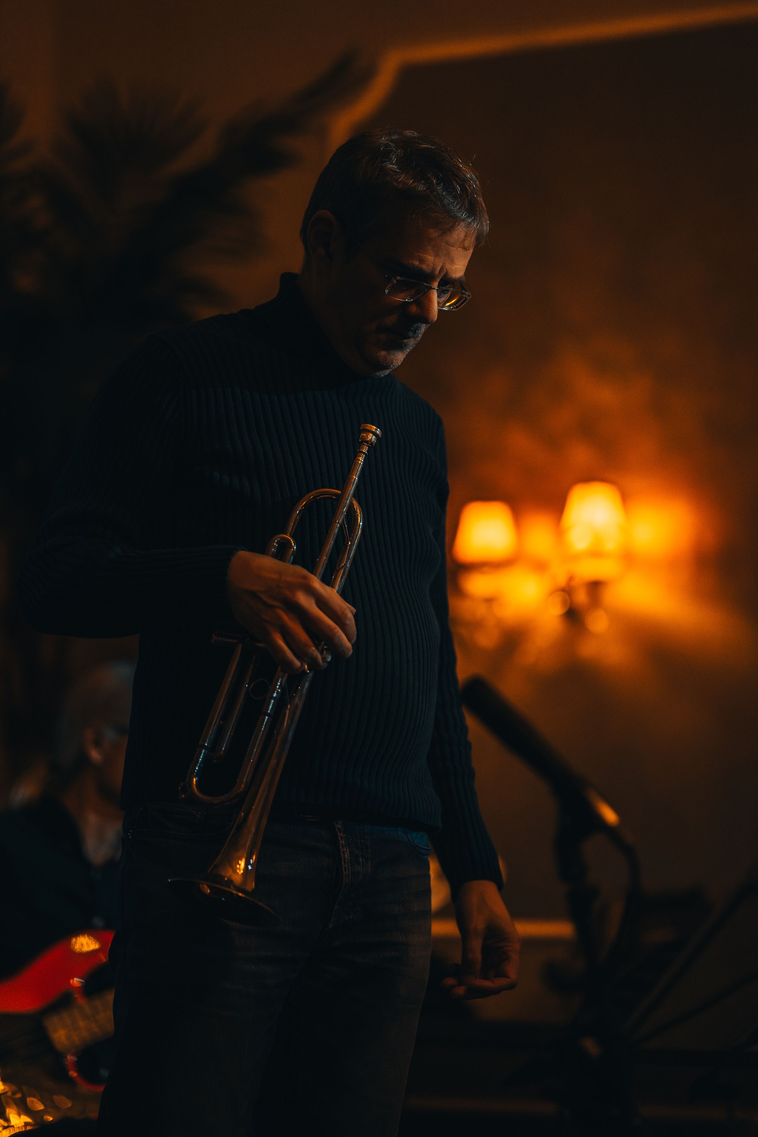 Trumpet player performs in silhouette against warm orange stage lighting.