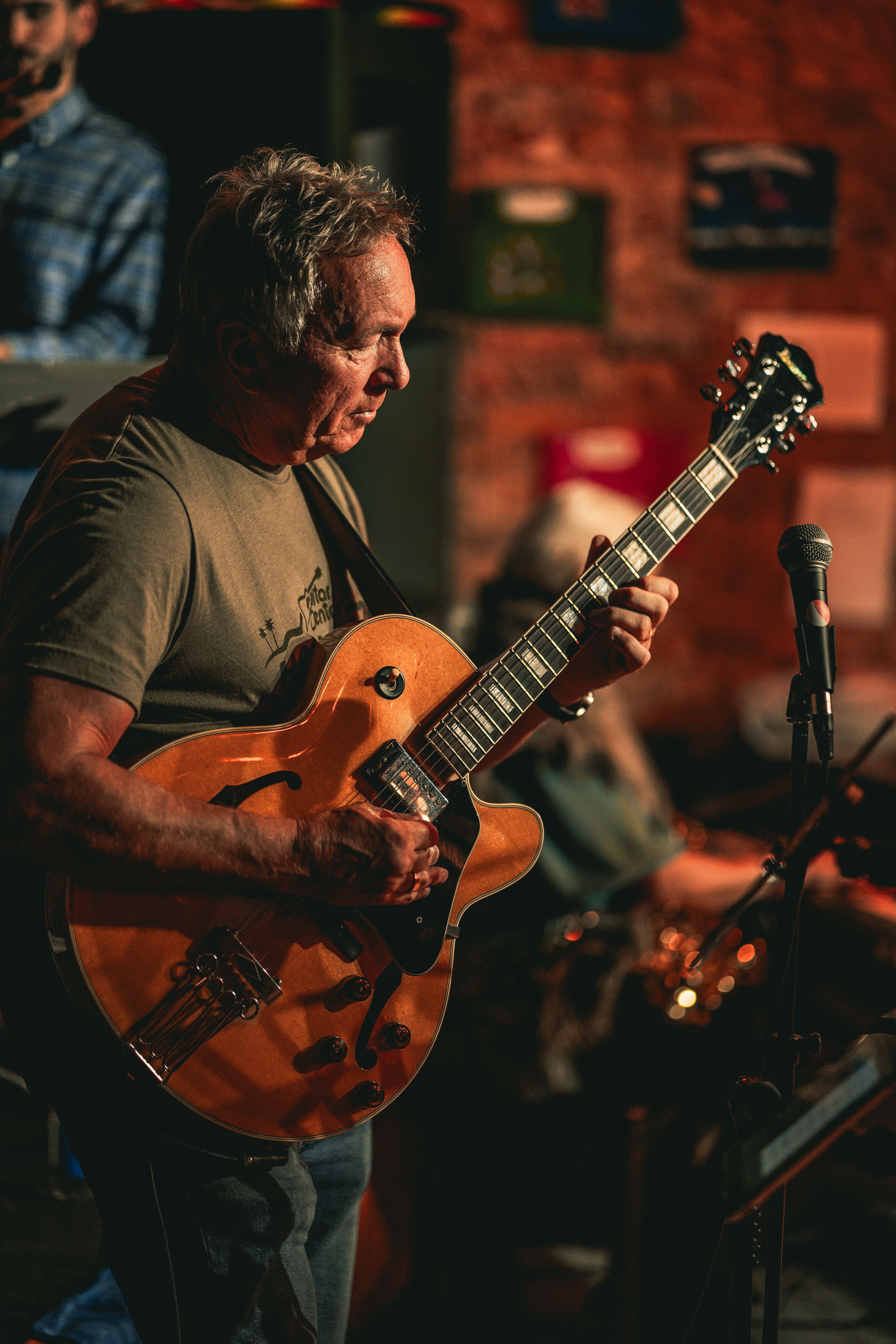 Guitarist playing an acoustic guitar during a live performance in a brick-walled venue.