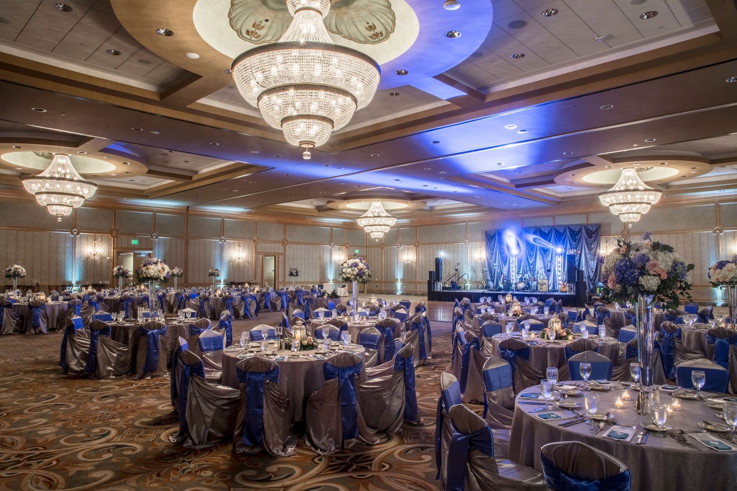 Elegant ballroom setup with crystal chandeliers and blue uplighting for wedding reception.