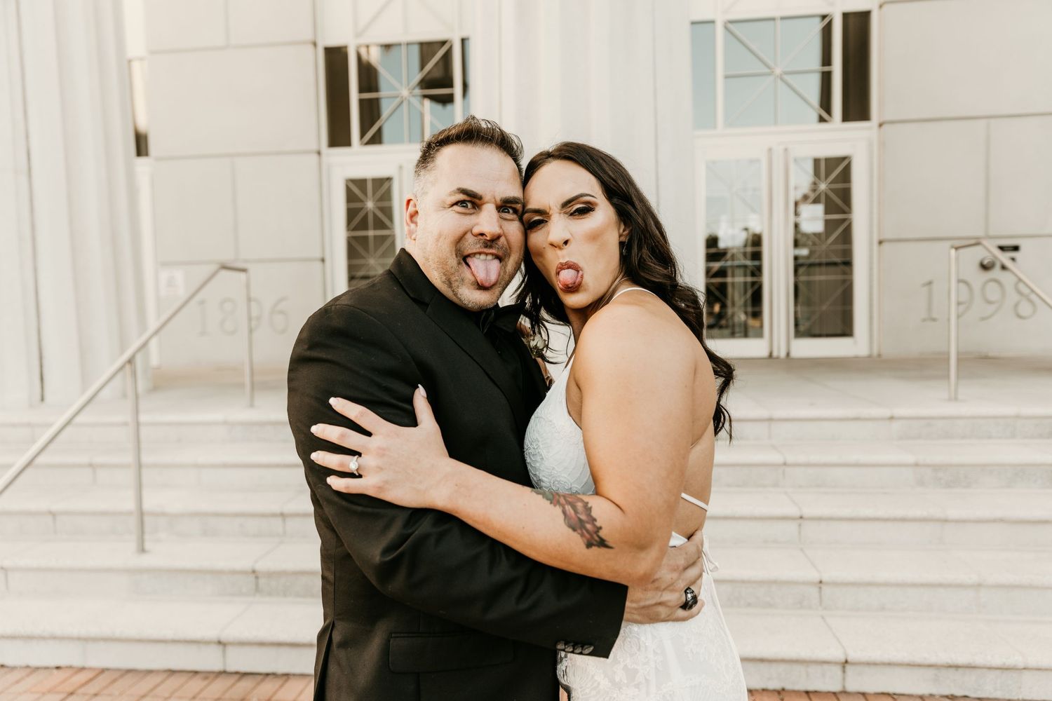 Happy couple embracing on white steps in formal attire.
