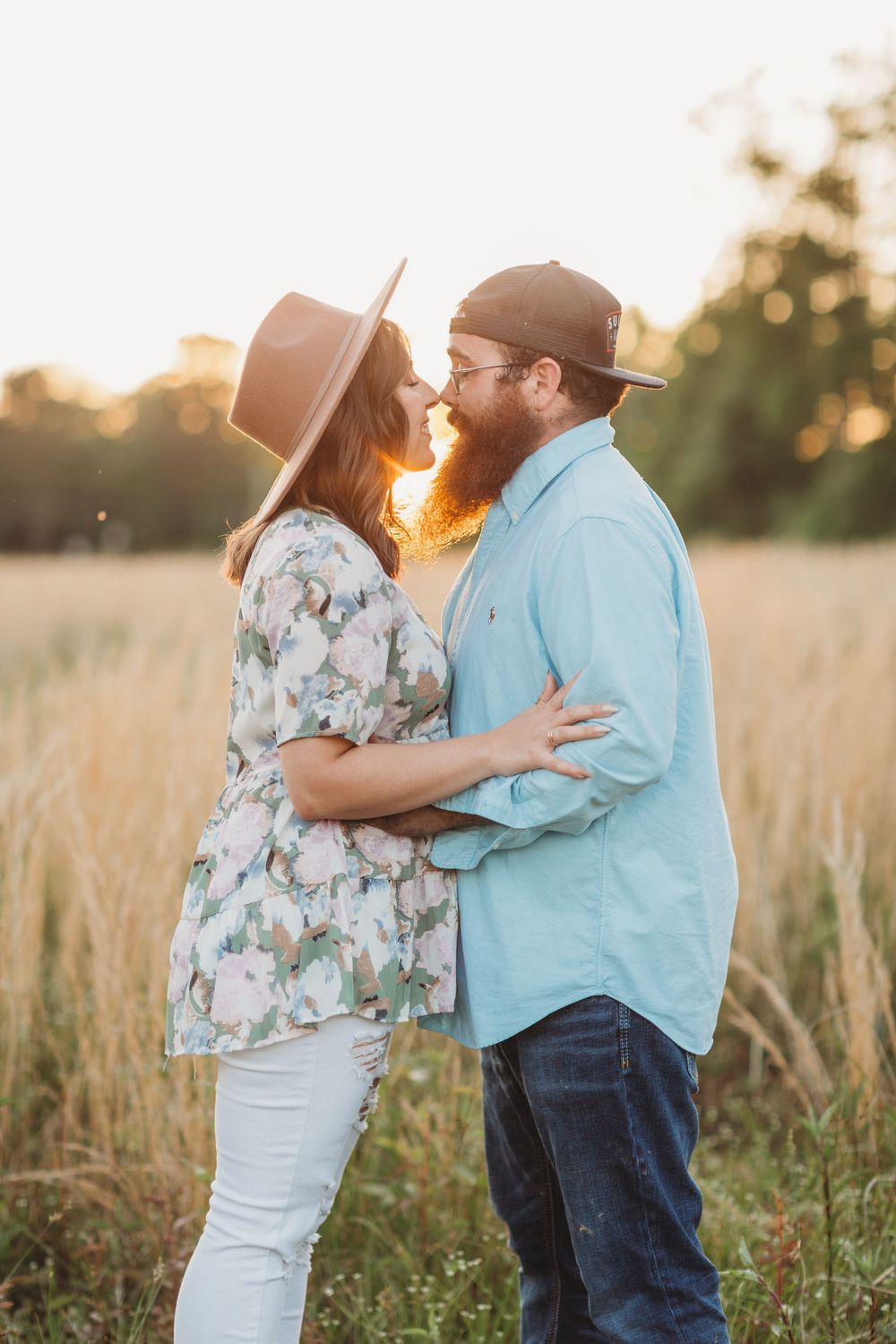 Romantic couple embracing in golden wheat field at sunset wearing casual attire.