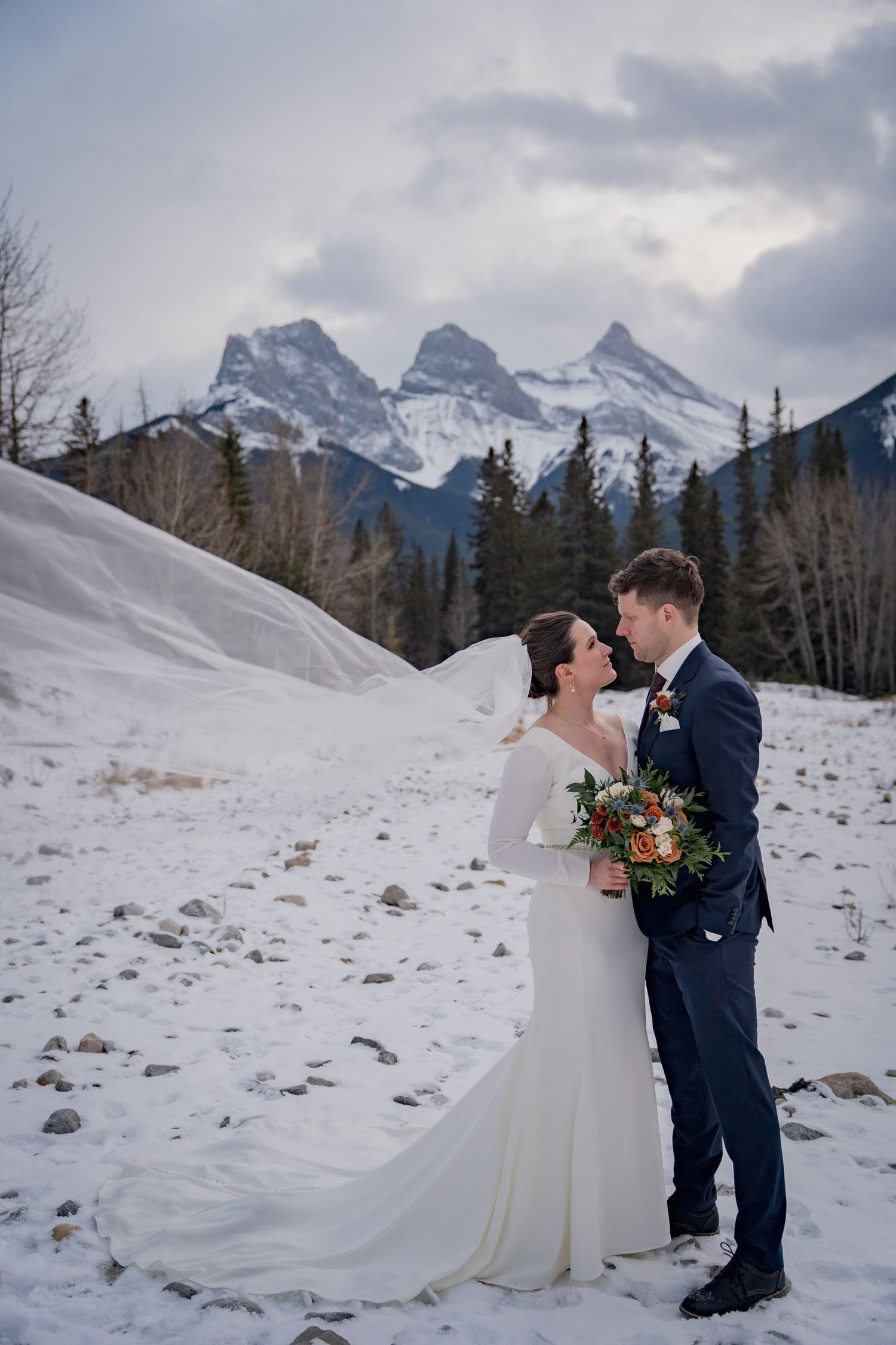 A winter wedding portrait with snow-capped Three Sisters mountains in the background.