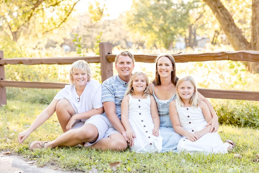 Family photo session showing playful interactions along a wooden fence in warm evening light.