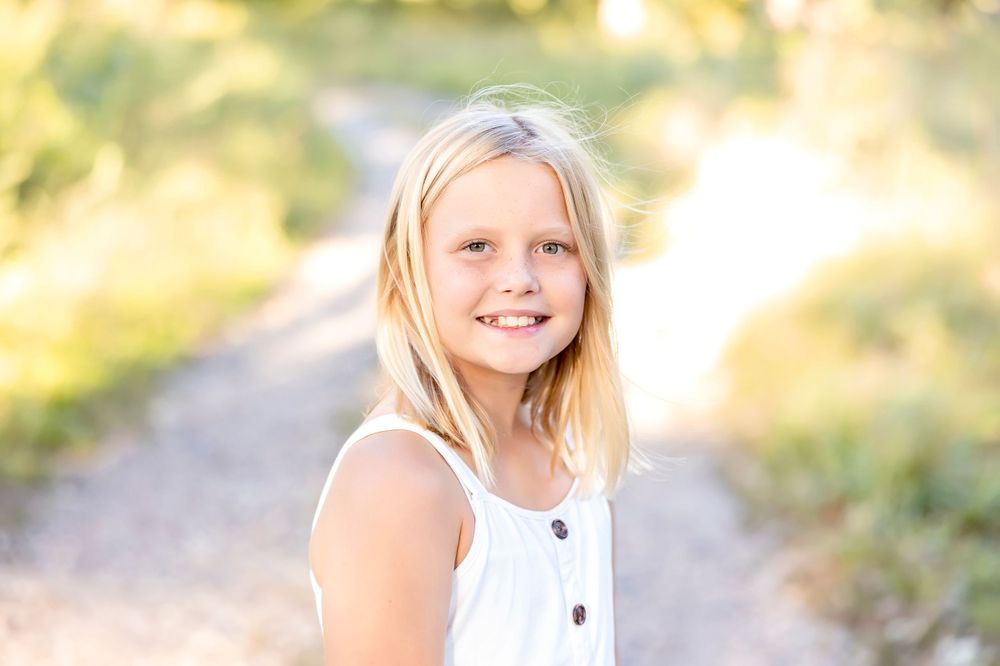 Child in white dress smiling brightly in golden outdoor lighting.