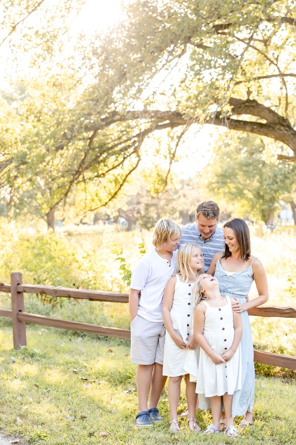 A joyful outdoor family photoshoot in a sun-drenched field with wooden fence during golden hour.