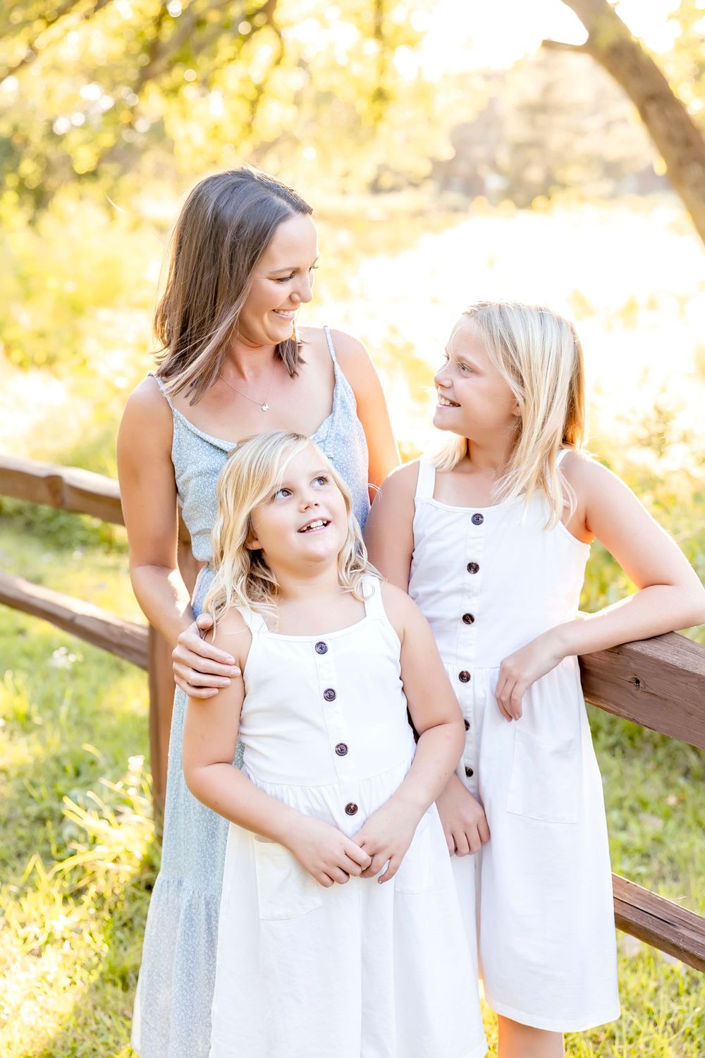 Three people in matching white dresses share laughter during outdoor photo session.