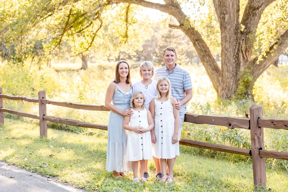 White-clad family members walk together on a path surrounded by golden-lit trees and wildflowers.