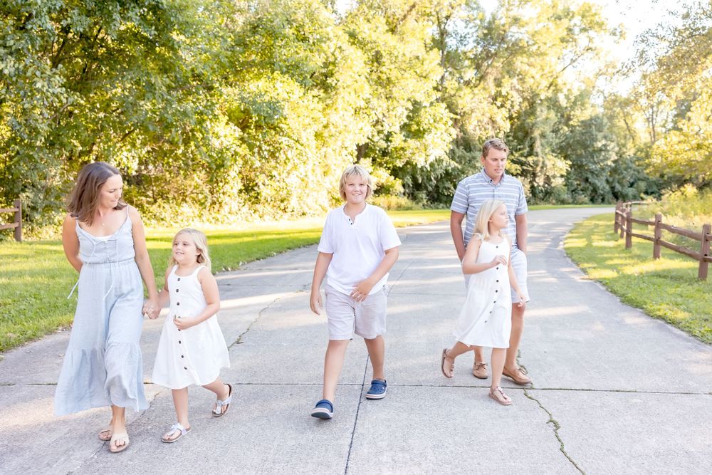 Family strolls along a paved pathway in coordinated white outfits during golden hour.
